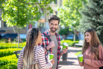 Three friends chatting drinking coffee while standing in park