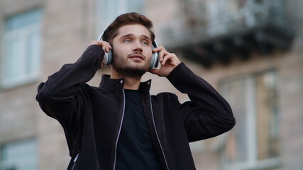 Happy guy listening music with headphones outdoors. Chherful man dancing outside