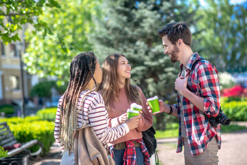 Tall guy and two long-haired girls with coffee in the square