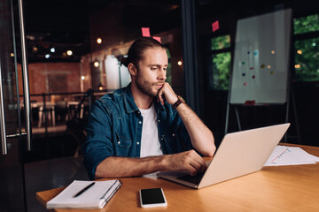 bearded businessman using laptop near notebook and smartphone with blank screen