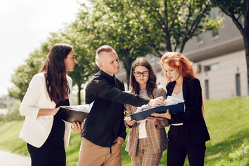 Business meeting of business partners outdoors on a sunny day. Young people, three women and a man are looking at documents, talking. Business ideas, deals, office work