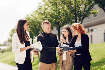 Business meeting of business partners outdoors on a sunny day. Young people, three women and a man are looking at documents, talking. Business ideas, deals, office work