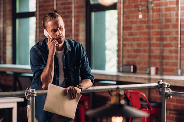 selective focus of bearded businessman talking on smartphone and holding folder in office
