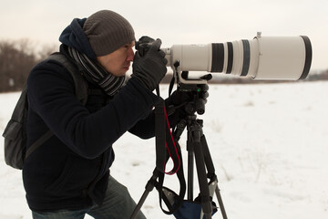 Photographer in winter with big zoom lens on the tripod 
