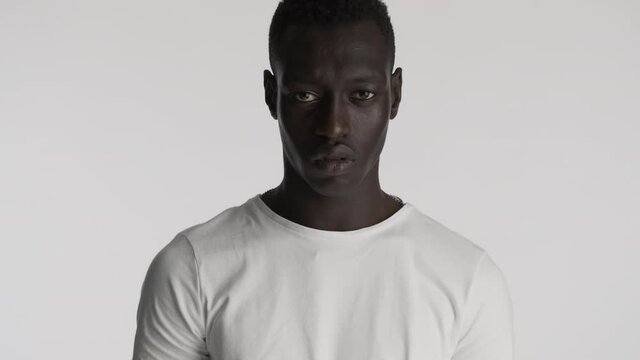 Portrait of serious African American man in white t-shirt aggressively looking in camera over gray background. Angry expression