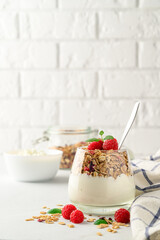 Parfait yogurt with granola and raspberries in a glass, light background, copy space. Healthy breakfast concept.