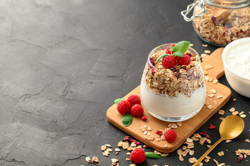 Parfait yogurt with granola and raspberries in a glass, black background, copy space. Healthy breakfast concept.
