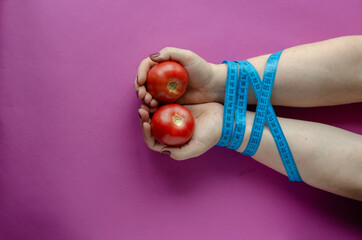 Female hands with ripe tomatoes are tied with measuring tape.