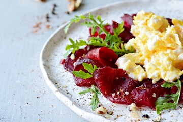 Scramble of eggs with carpaccio of baked beets with walnuts, aromatic herbs and arugula on a plate. Delicious healthy breakfast.  Beet carpaccio with sauce on a white plate.