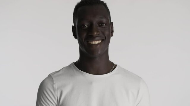 Handsome African American guy in white t-shirt happily looking in camera over gray background