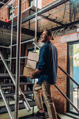 selective focus of smiling businessman holding boxes while walking on stairs in office