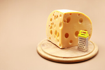 Big piece of cheese with small toy grater with copy space isolated on brown background 