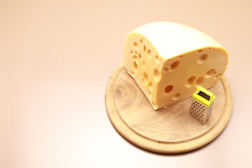 Big piece of cheese with small toy grater with copy space isolated on brown background 