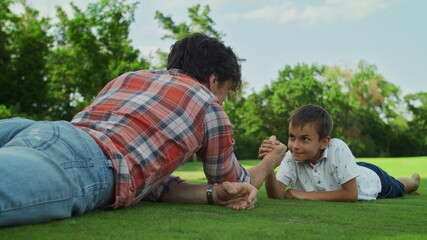Naklejka na ściany i meble Father and son practising arm wrestling in meadow. Boy winning competition