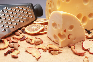 big piece of cheese, nuts mix and  dry fruits with steel grater on wooden cutting board isolated on gray background