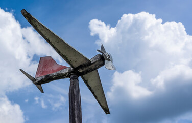 Shaped like plane weather vane made of scrap materials against cloudy sky