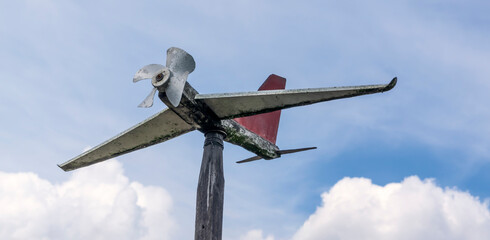 Shaped like plane weather vane made of scrap materials against cloudy sky