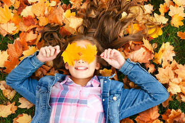Autumn portrait of happy smiling little girl child lying in leaves and closing her eyes with leaves in the park - 365234571