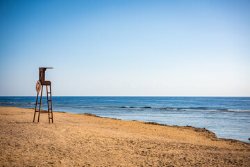 Empty beach at sunset with lifeguard seat in Egypt. Wooden chairs on the beach at dusk