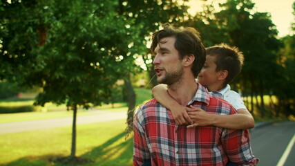 Father giving son piggyback riding in park. Man and boy talking on street