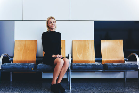 Smiling female student waiting for classmates in hallway before start lectures in University, charming woman dressed in elegant clothes sitting in office interior before meeting with entrepreneur