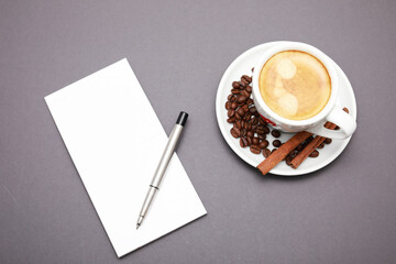White cup of coffee, around beans, note book and pen isolated  gray background.