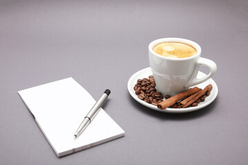 White cup of coffee, around beans, note book and pen isolated  gray background.