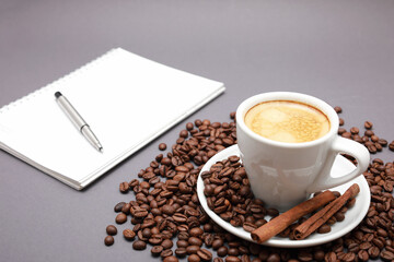 White cup of coffee, around beans, note book and pen isolated  gray background.