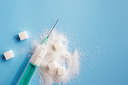 Granulated sugar, sugar cubes and syringe on blue backgroud.