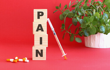 The words PAIN is made of wooden cubes on a red background with medical drugs. Medical concept.