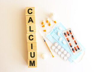 The words CALCIUM is made of wooden cubes on a white background with medical drugs and medical mask. Medical concept.