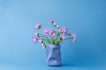 a bouquet of purple Daisy flowers in a vase from under a can of Cola on a blue background