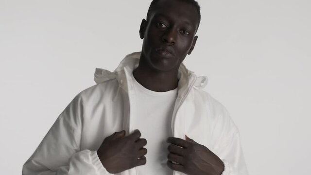 Handsome stylish African American guy in white jacket confidently posing on camera over gray background. Serious expression