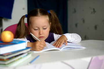 caucasian child girl student sits at a table and writes in a notebook with light smile