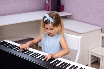 a charming six year old blonde girl in a blue dress plays the piano in her bedroom