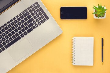 notebook, laptop, pen, flower, mobile phone on a yellow surface