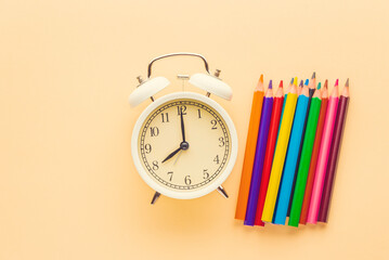White alarm clock and color pencils on a yellow background