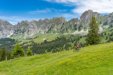 Fototapeta na wymiar active senior woman riding her electric mountain bike below the seven summits of Churfirsten in Canton St. Gallen, Switzerland, landscape