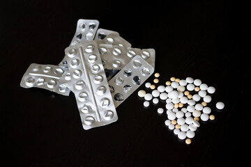 Tablets of various sizes, pulled out of blisters and scattered on a black table, next to empty blisters.
