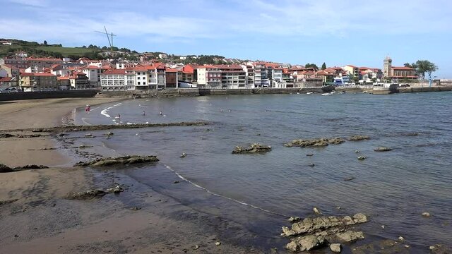 Village on the coast of the Cantabrian Sea. The church tower at one end and people bathing in the sea. Luanco Asturias. Spain