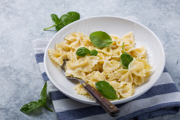 Curly bow-shaped paste with basil on concrete table