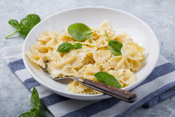 Curly bow-shaped paste with basil on concrete table