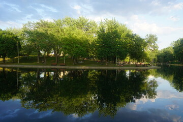 Montreal, QC / Canada - 7/3/2020: reflections of trees and clouds on lake water, La Fontaine Park.