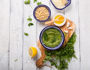 Homemade parsley pesto sauce and ingredients on white  wooden background.