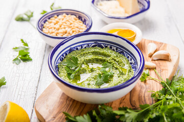Homemade parsley pesto sauce and ingredients on white  wooden background.