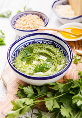 Homemade parsley pesto sauce and ingredients on white  wooden background.