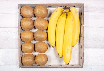 Bananas and kiwis placed in an old wooden tray on a background of old wooden floor