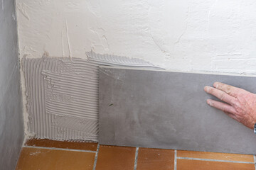 the tiler lays a ceramic tile on the wall