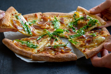 Pizza. People are eating pizza. Hot pizza cut into pieces. Pizza with jamon, cheese, arugula, pine nuts and pear. A party. Fast food. People are sorting out pizza. People sort out food