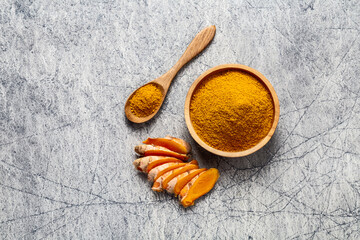 Turmeric powder and fresh turmeric root on grey concrete background.